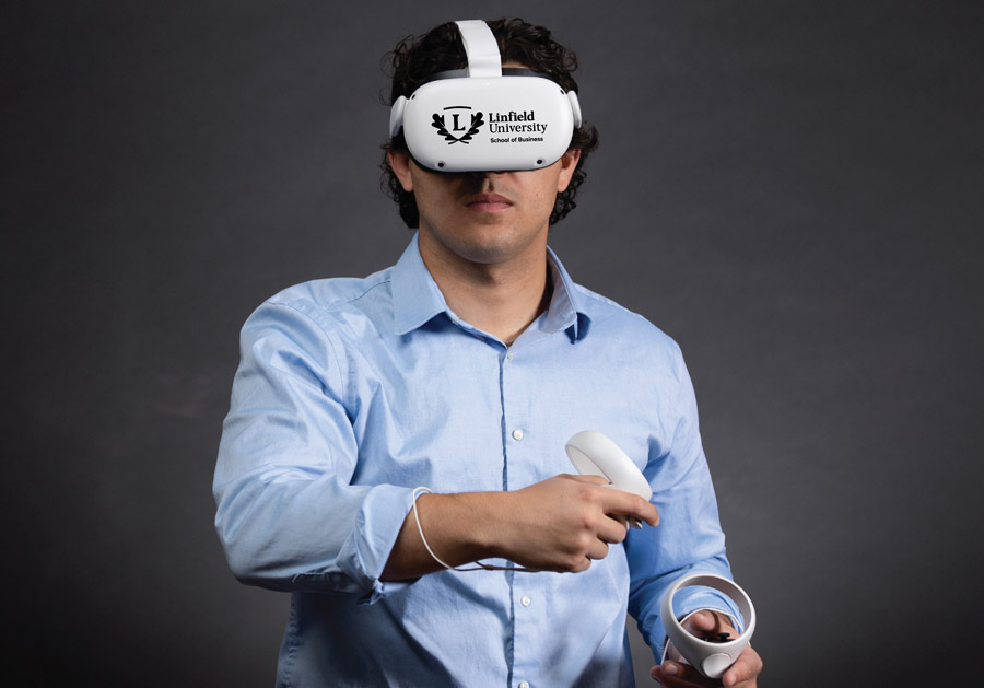 Linfield business student wearing Linfield-branded Oculus headset and holding two hand controllers.