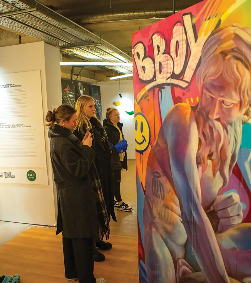 Students view an art exhibit about the history of sports in Paris, France.