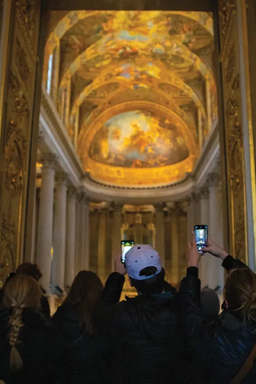 Students visit the Palace of Versailles and take photos of the ceiling with their phones.