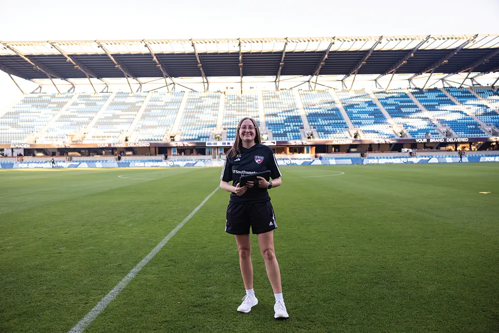 Katelyn standing on a soccer pitch holding a tablet.