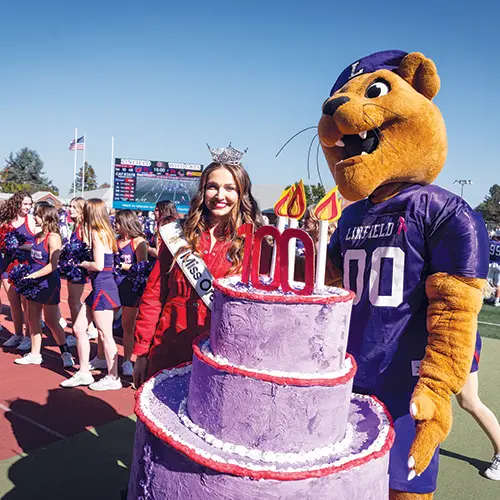 Mack the Wildcat and Miss Oregon standing next to Mack's 100 year birthday cake.