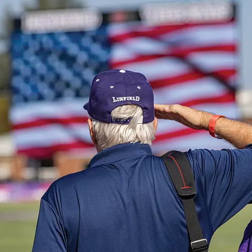 person wearing a Linfield hat saluting the flag during the National Anthem.