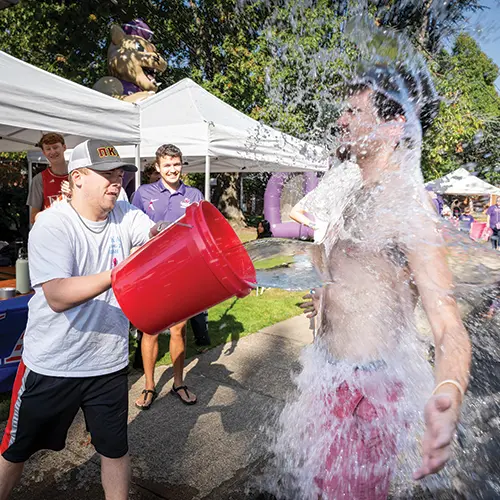 a student dumping a bucket of water on another student.