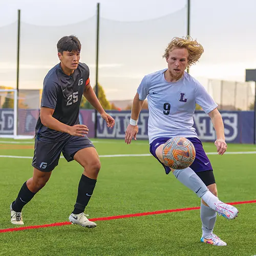 a Linfield soccer player going after the ball next to a George Fox player.